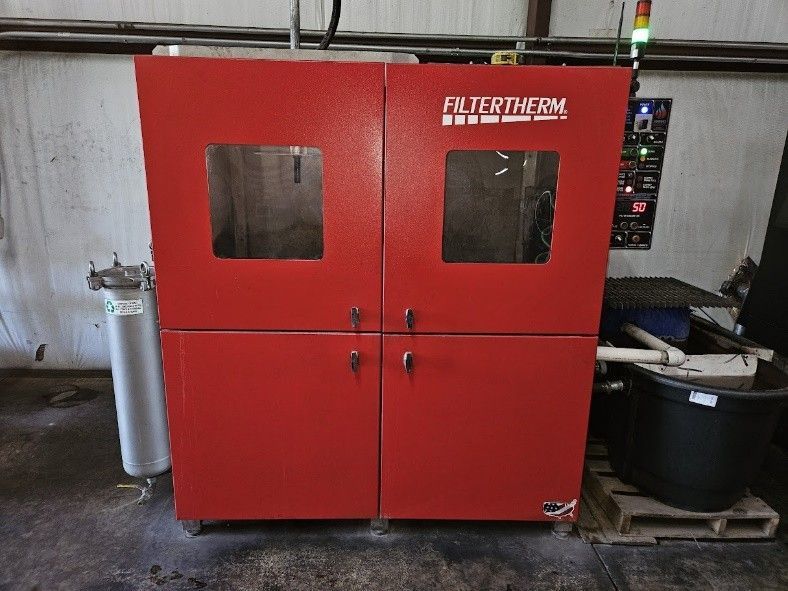 A red industrial Filtertherm machine with glass viewing windows, positioned in a workshop next to a filter and bucket.