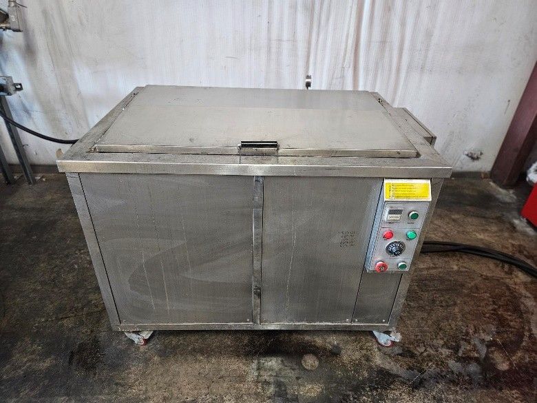 A stainless steel industrial ultrasonic cleaner unit on wheels with a control panel on the right side.
