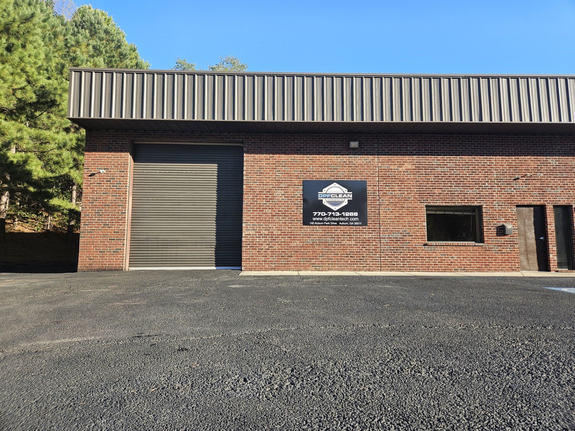 A brick warehouse building with a large roll-up garage door, a prominent sign, and a gravel parking lot.