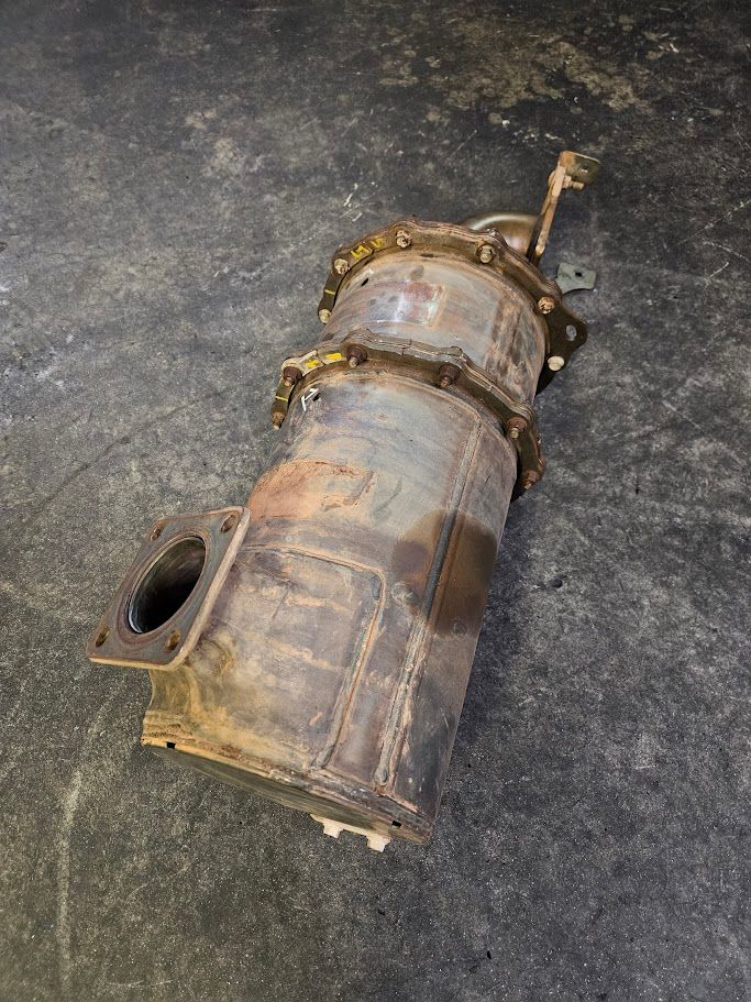 A large, rusted metal catalytic converter or diesel particulate filter resting on a gray concrete floor.