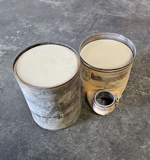 Two cylindrical industrial filters resting on a gray concrete floor; one has a honeycomb pattern and the other is solid.