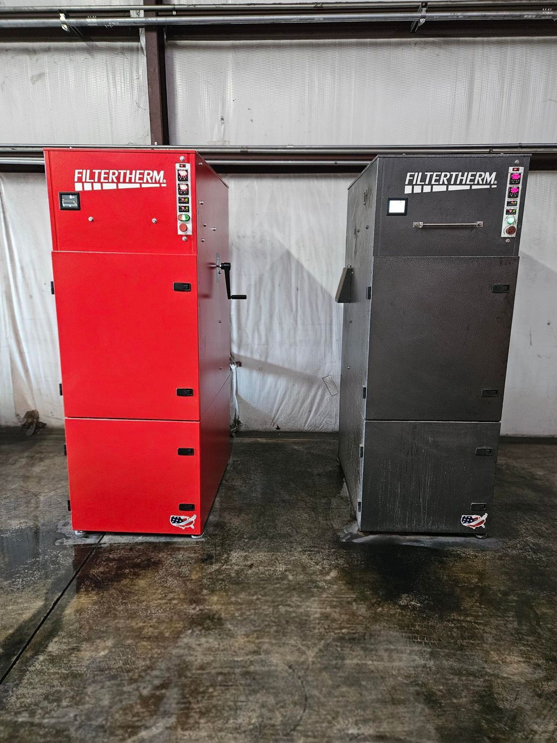 Two industrial heaters, one red and one black, standing side-by-side on a concrete floor in an indoor warehouse setting.