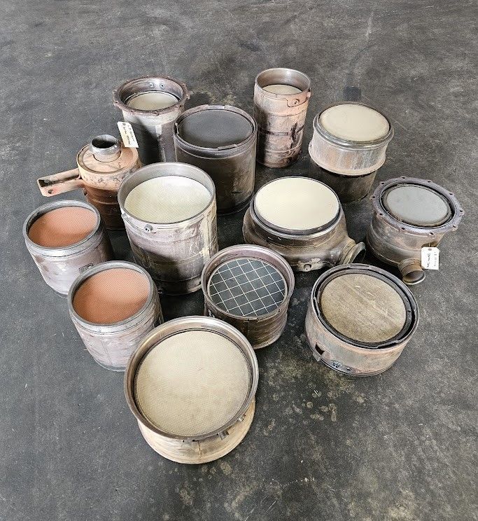 An assortment of cylindrical metal automotive catalytic converters arranged on a concrete floor.