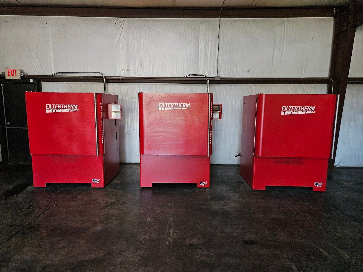 Three identical red, box-shaped industrial furnaces sit side-by-side in a garage-like space with white walls.