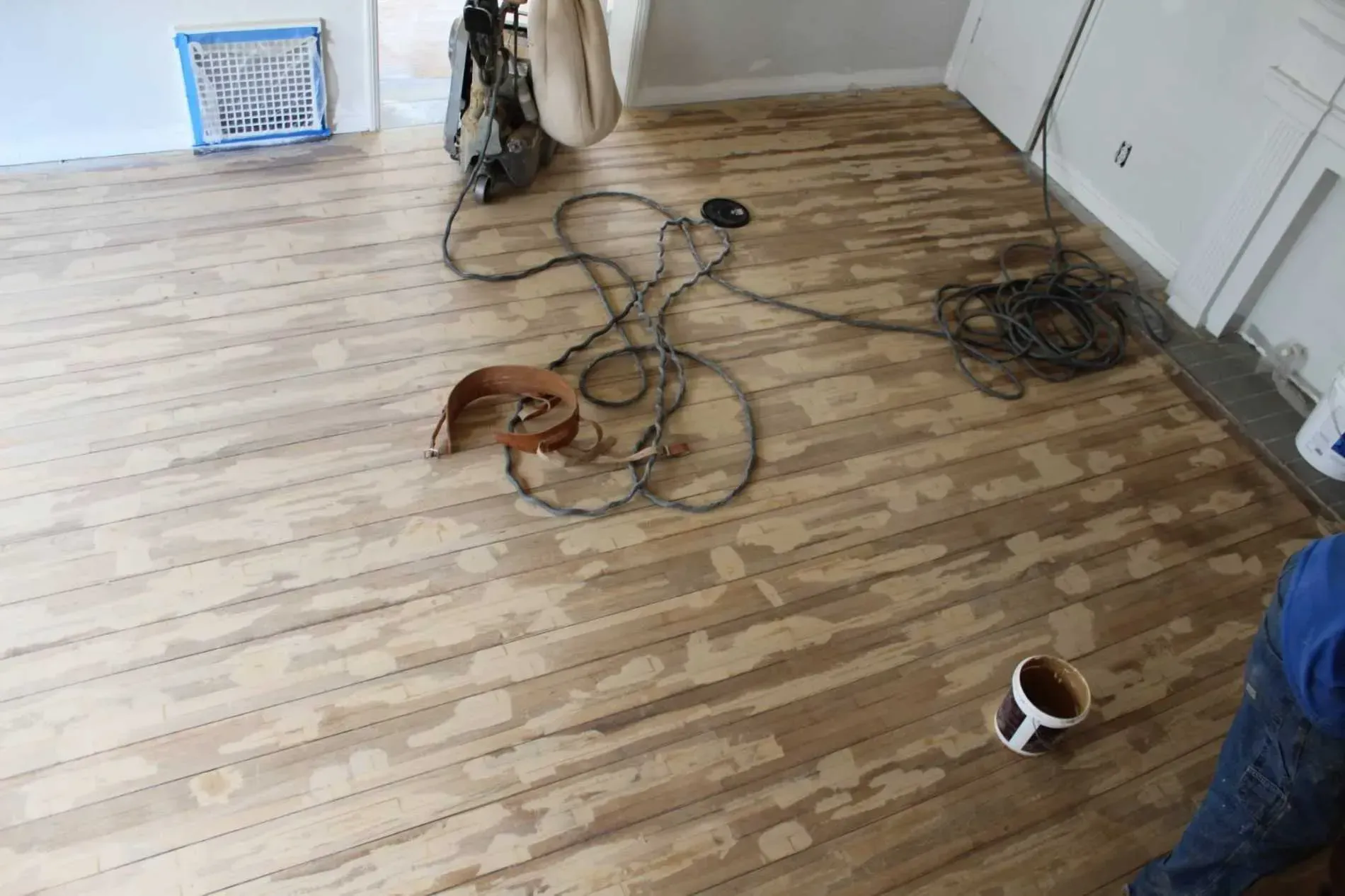 A person is sanding a wooden floor with a vacuum cleaner.