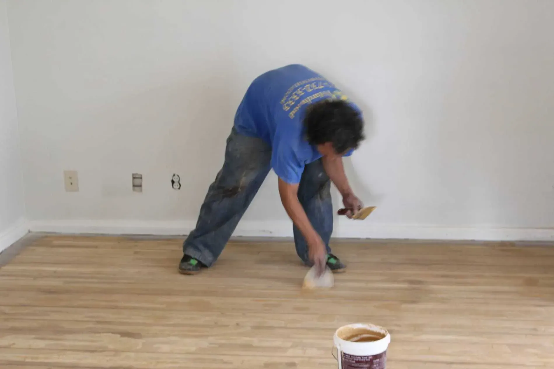 A man in a blue shirt is painting a wooden floor