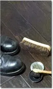 A pair of black shoes are sitting on a wooden floor next to a brush and polish.