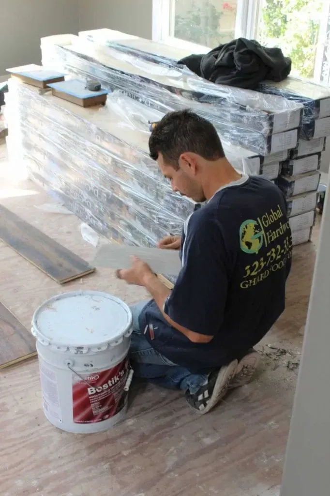 A man is kneeling down next to a bucket of paint.