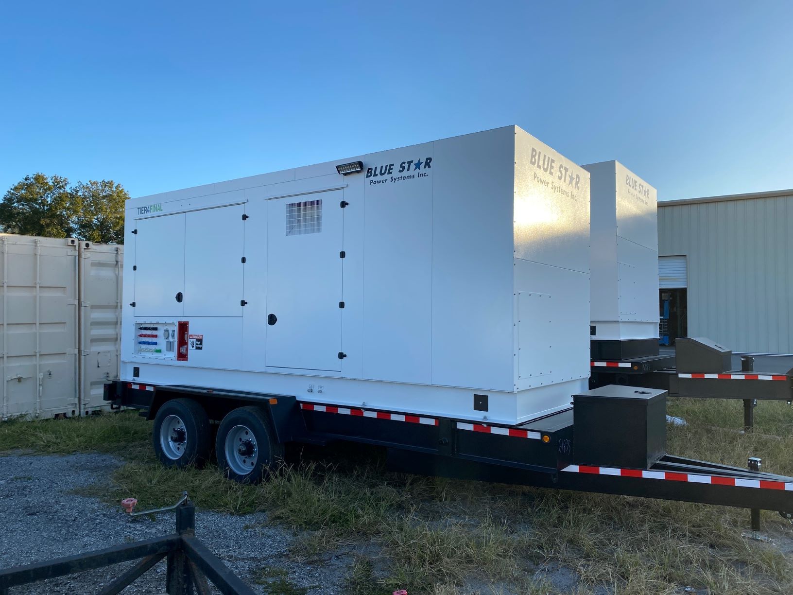 White industrial generator on a dual-axle trailer parked beside a warehouse in a gravel lot.