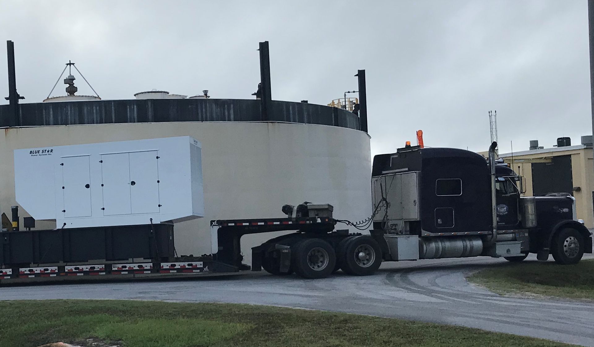 Large white industrial tank loaded on a flatbed semi truck on a wet road under cloudy skies