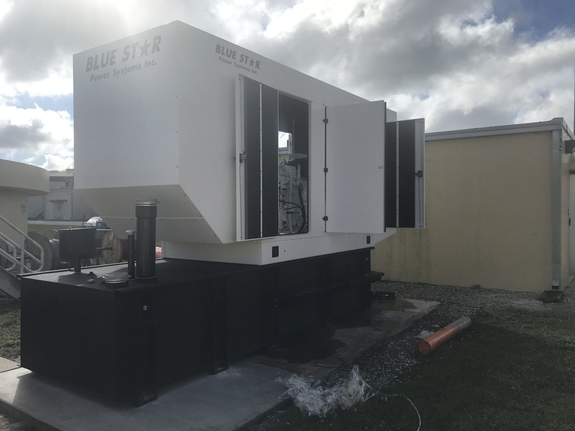 Large white industrial machine on a black base outdoors, with open doors and cloudy sky overhead