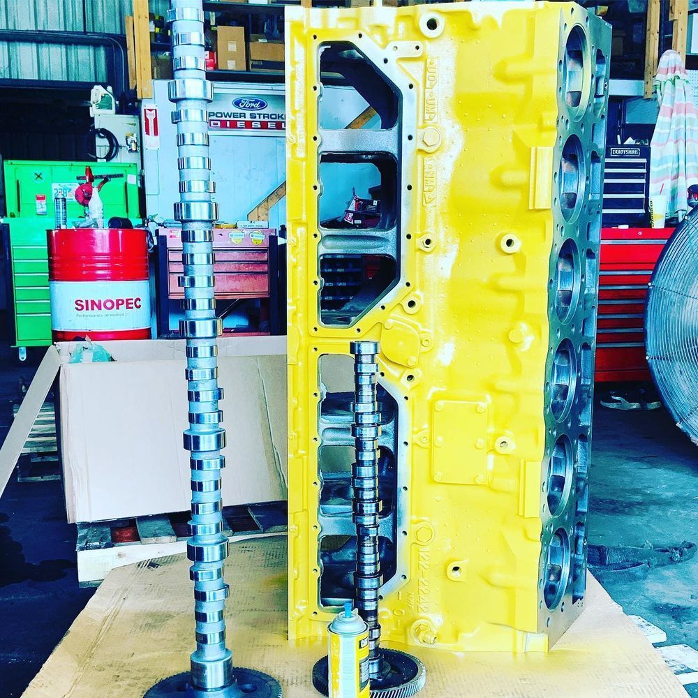 Yellow engine block in a workshop with two tall metal camshafts in front
