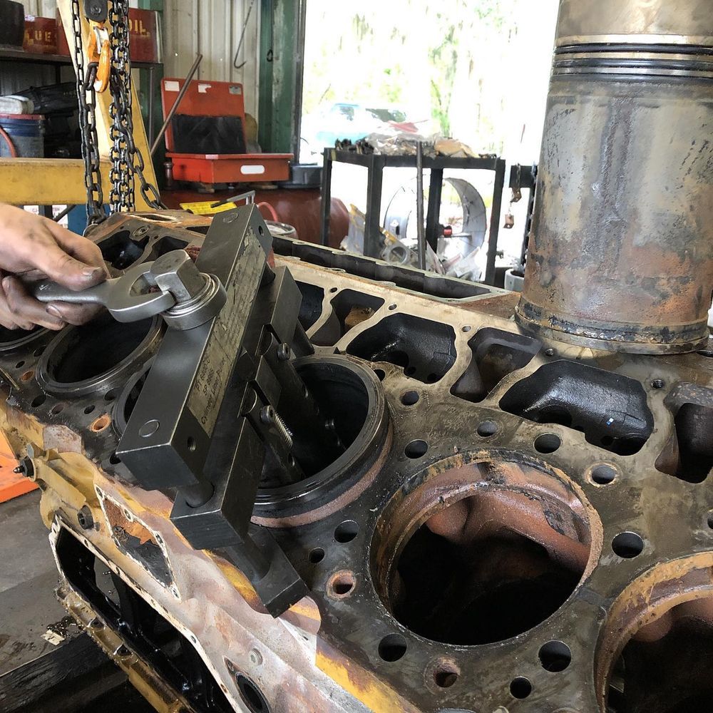 Hand using a wrench on a large disassembled engine block in a workshop