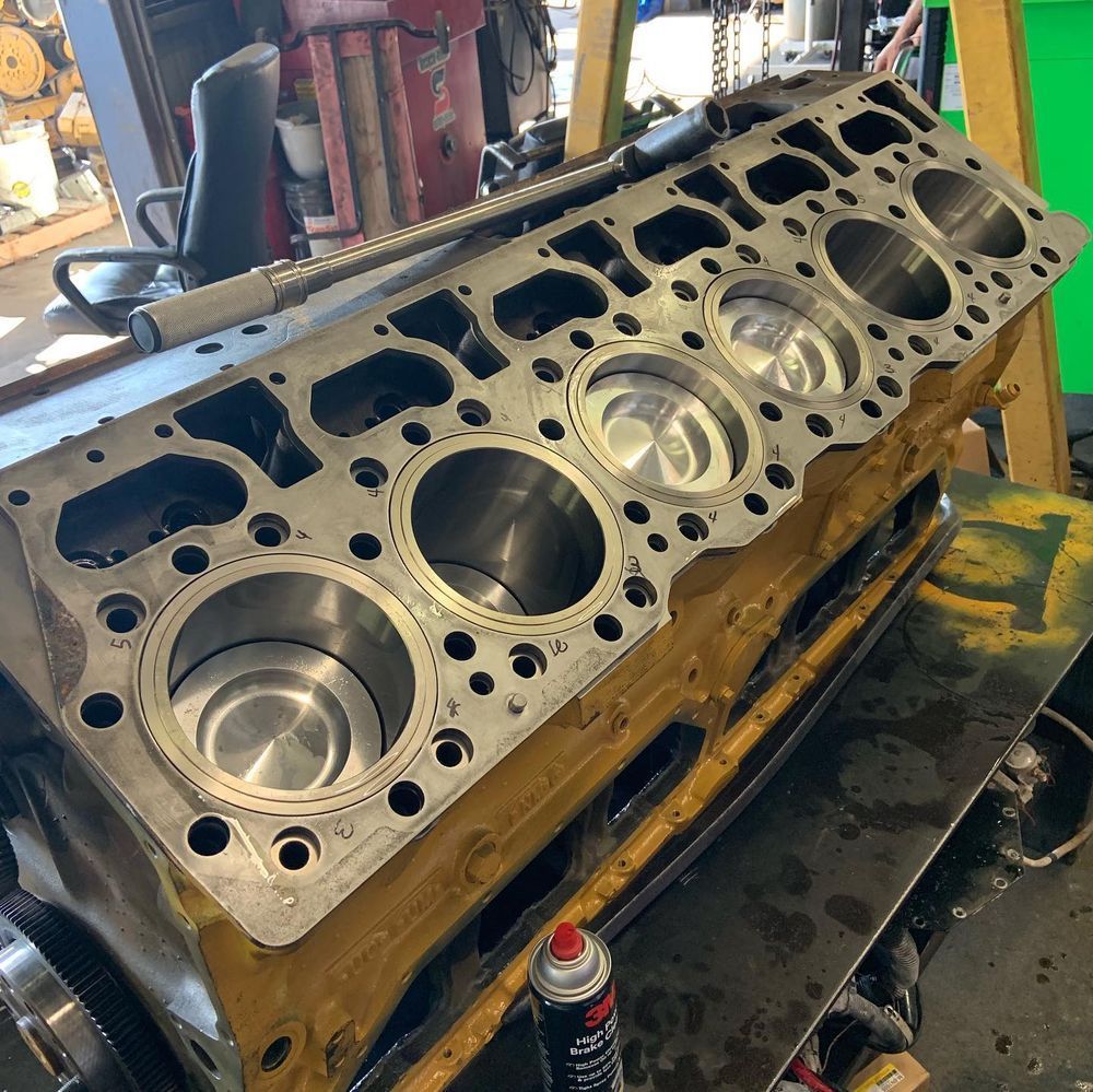 Machined engine block on a workshop bench, with visible cylinder bores and metal tools nearby