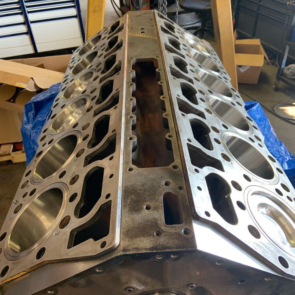 Engine block with cylinder heads removed, shown on a workshop bench in a garage.