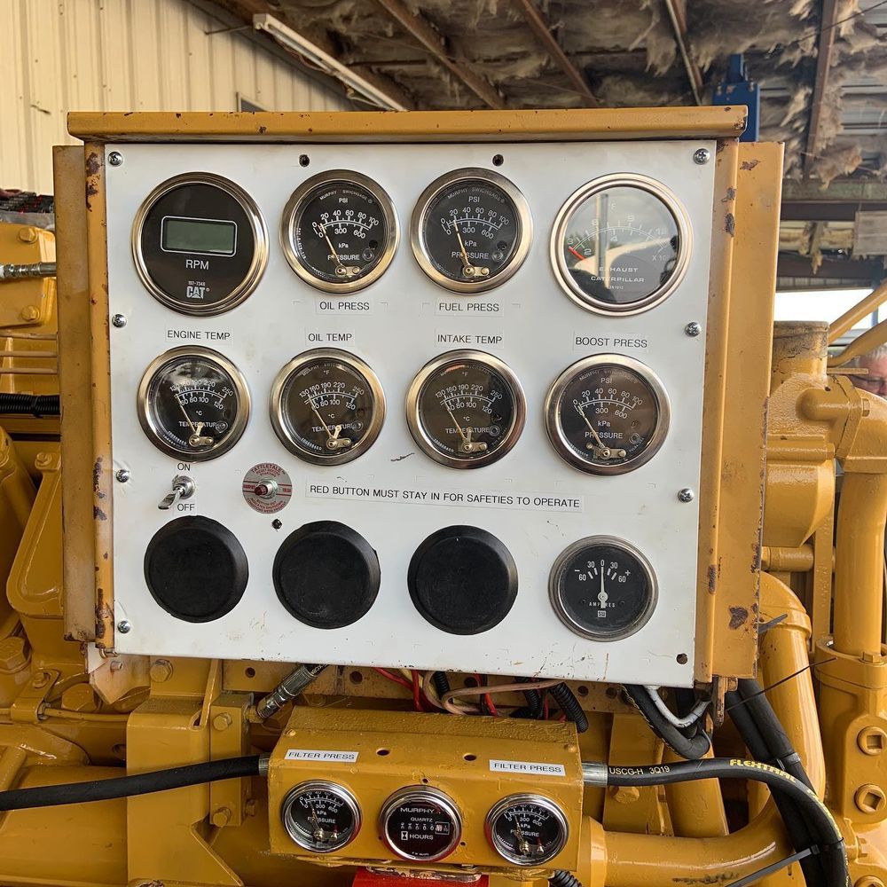 White industrial control panel with gauges and dials mounted on yellow machinery inside a workshop
