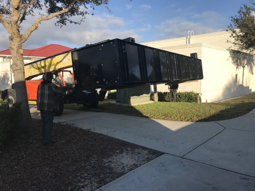 Worker guiding a large black dumpster across a driveway beside a house