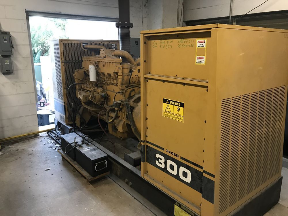 Yellow industrial generator in a garage, with engine components exposed and a “300” label on the side.