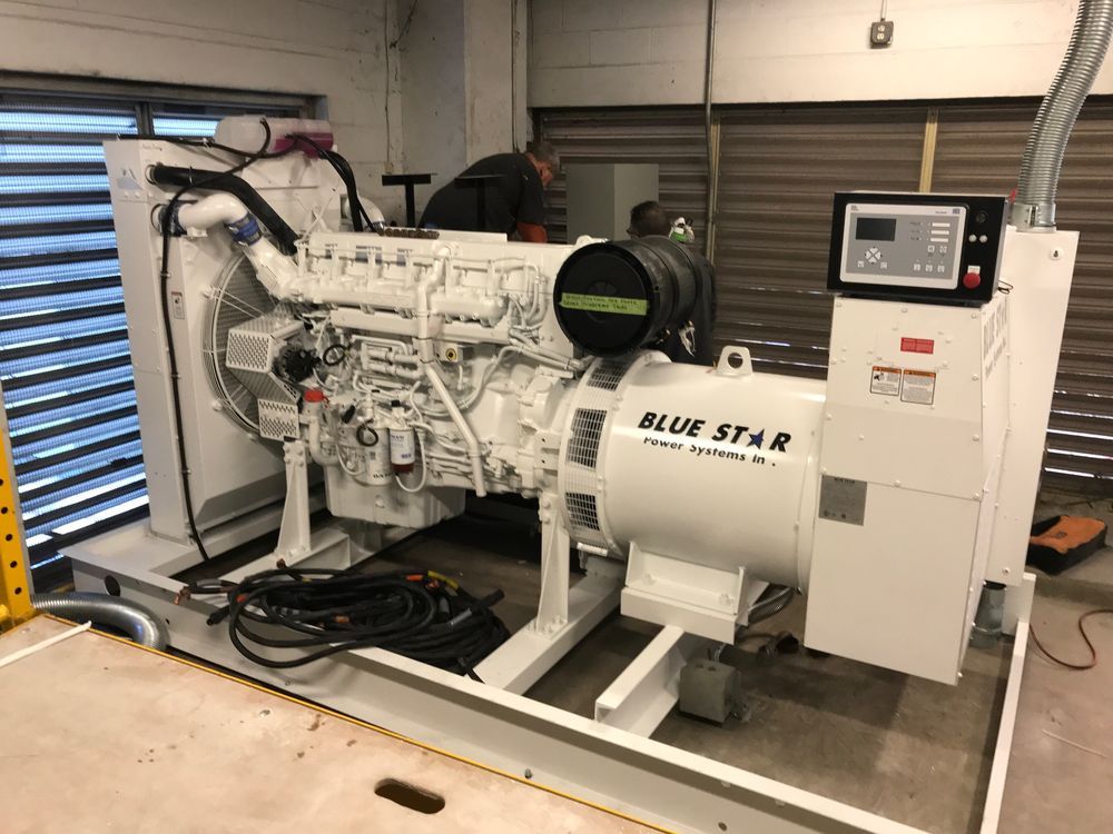 Large white generator set in an industrial bay with control panel and fuel tank, mounted on a metal frame.