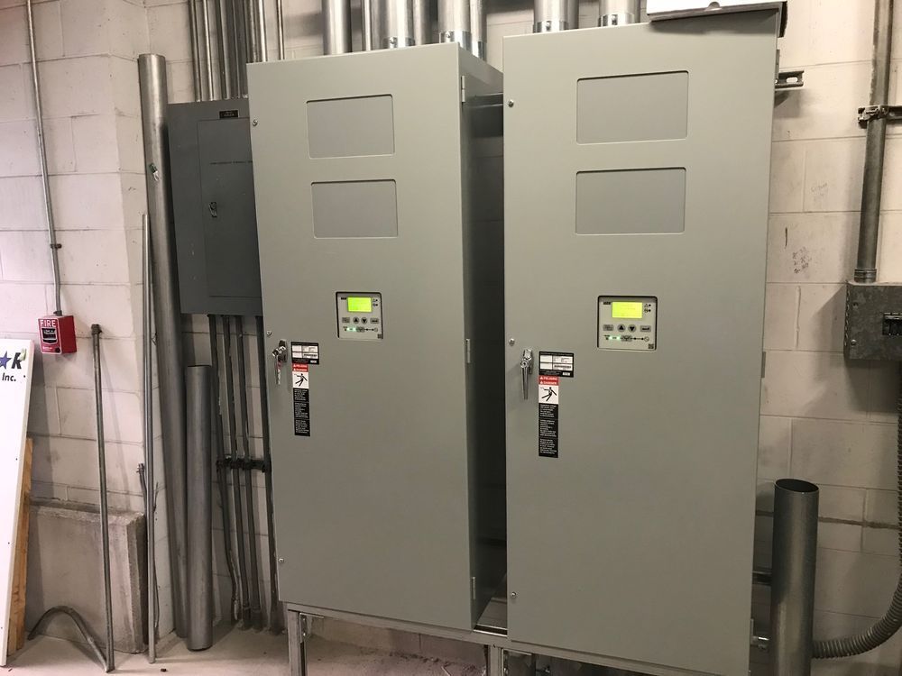 Two gray electrical control panels in an industrial room with exposed pipes and conduit