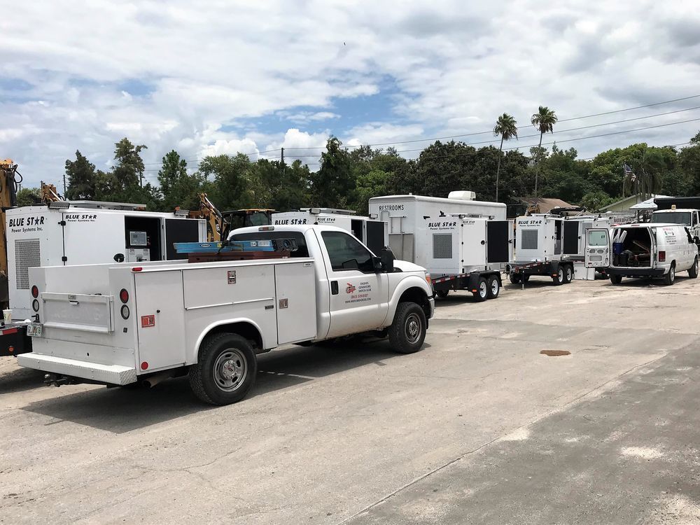 White utility trucks and trailers lined up on a dirt road under a cloudy sky.