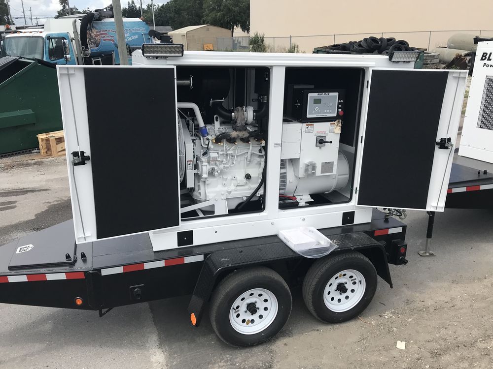 White utility trailer with open black doors showing industrial machinery inside, parked outdoors on a street