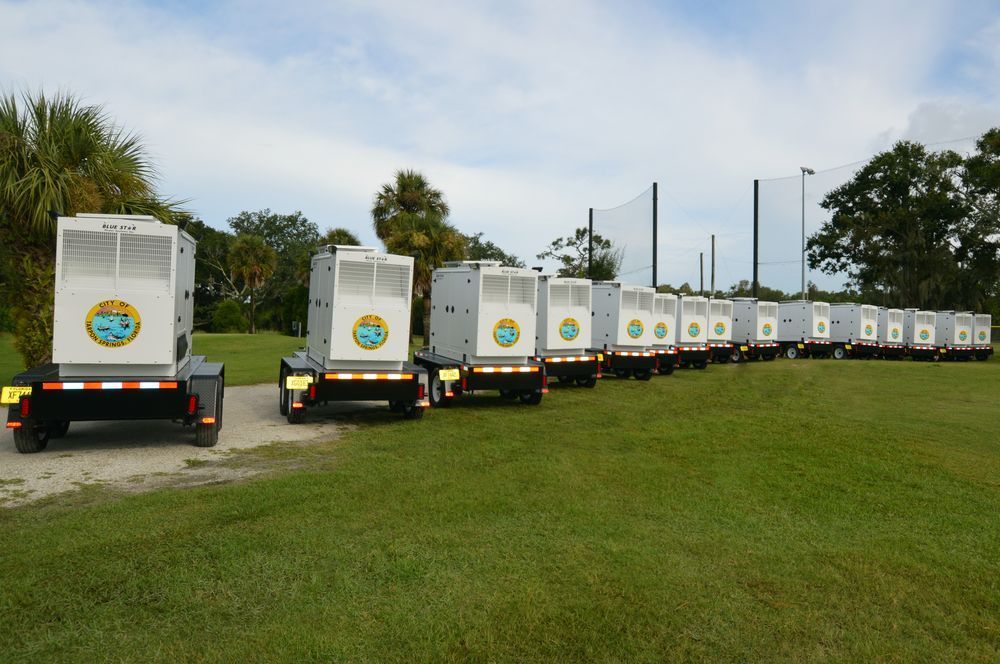 Line of white utility trailers with logos parked along a grassy road under a cloudy sky.