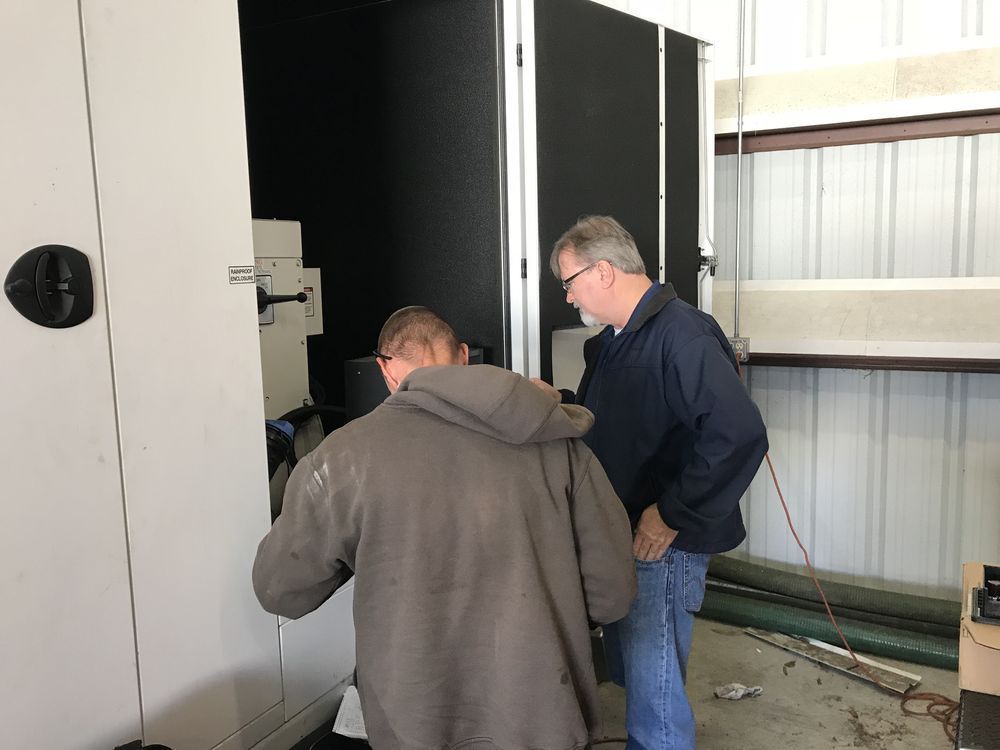 Two men inspect a black electrical cabinet in a workshop.