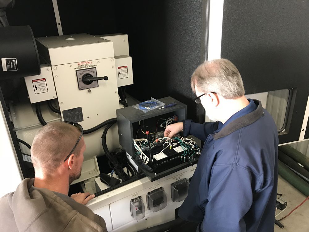 Two people inspect wiring inside an open industrial machine in a workshop.