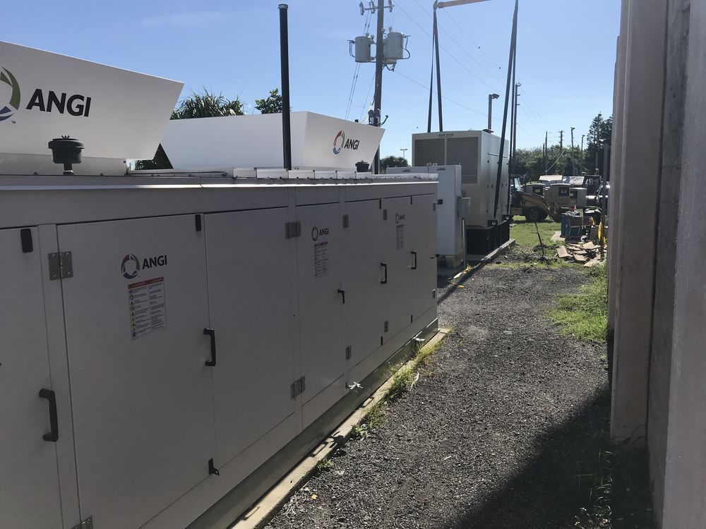 Row of white industrial generator units beside a gravel path under a clear sky
