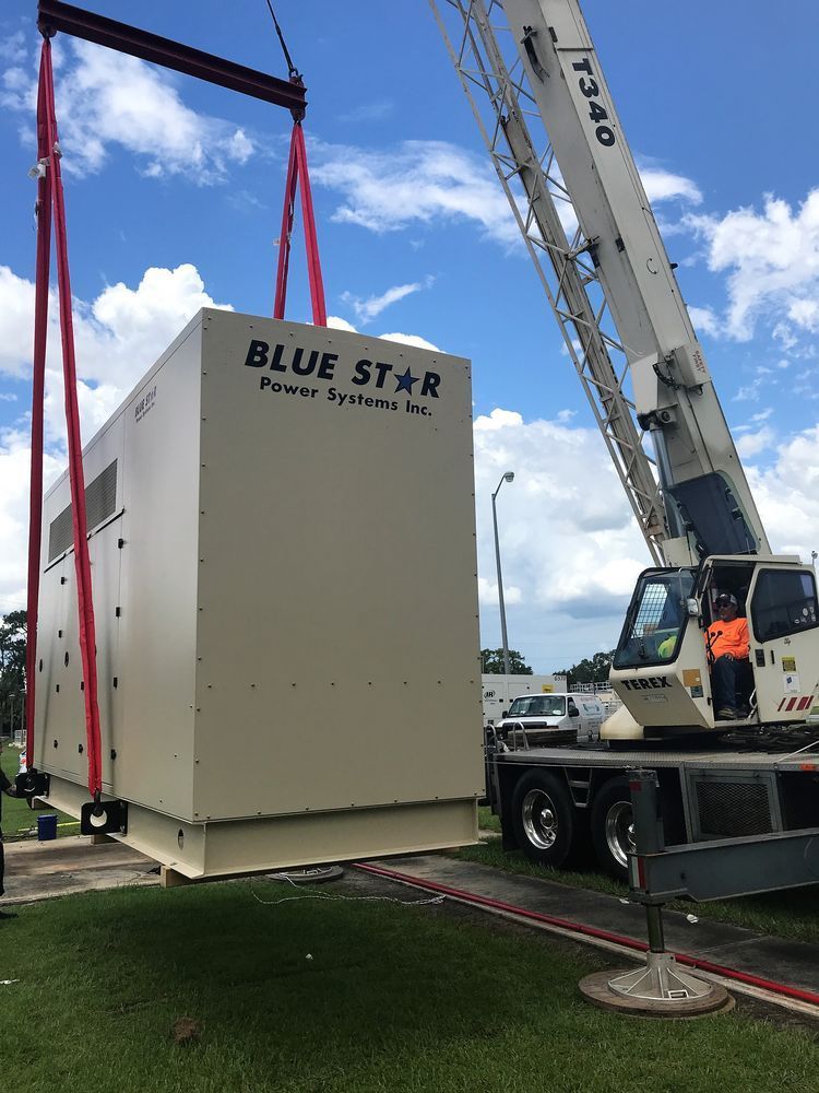 Crane lifting a large white Blue Star container onto a truck outdoors under a blue sky.