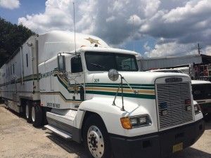 White semi-truck with green stripes parked outdoors under cloudy skies.