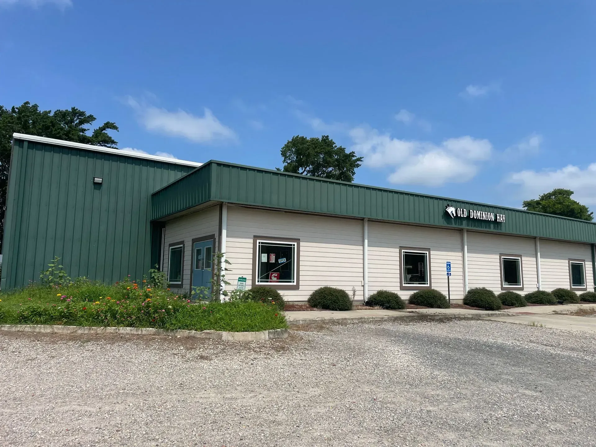 Green and white commercial building with sign under blue sky and gravel parking area.