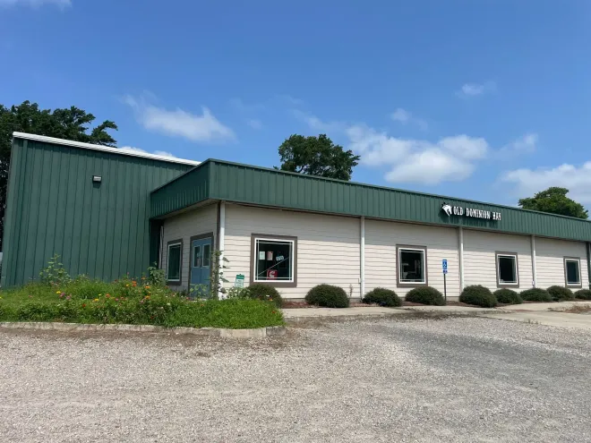 Green and white commercial building with sign under blue sky and gravel parking area.