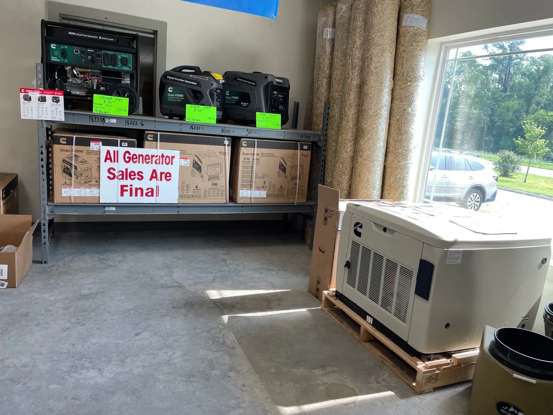 Interior of a store with generators for sale; some on a shelf, one on a pallet near a window.