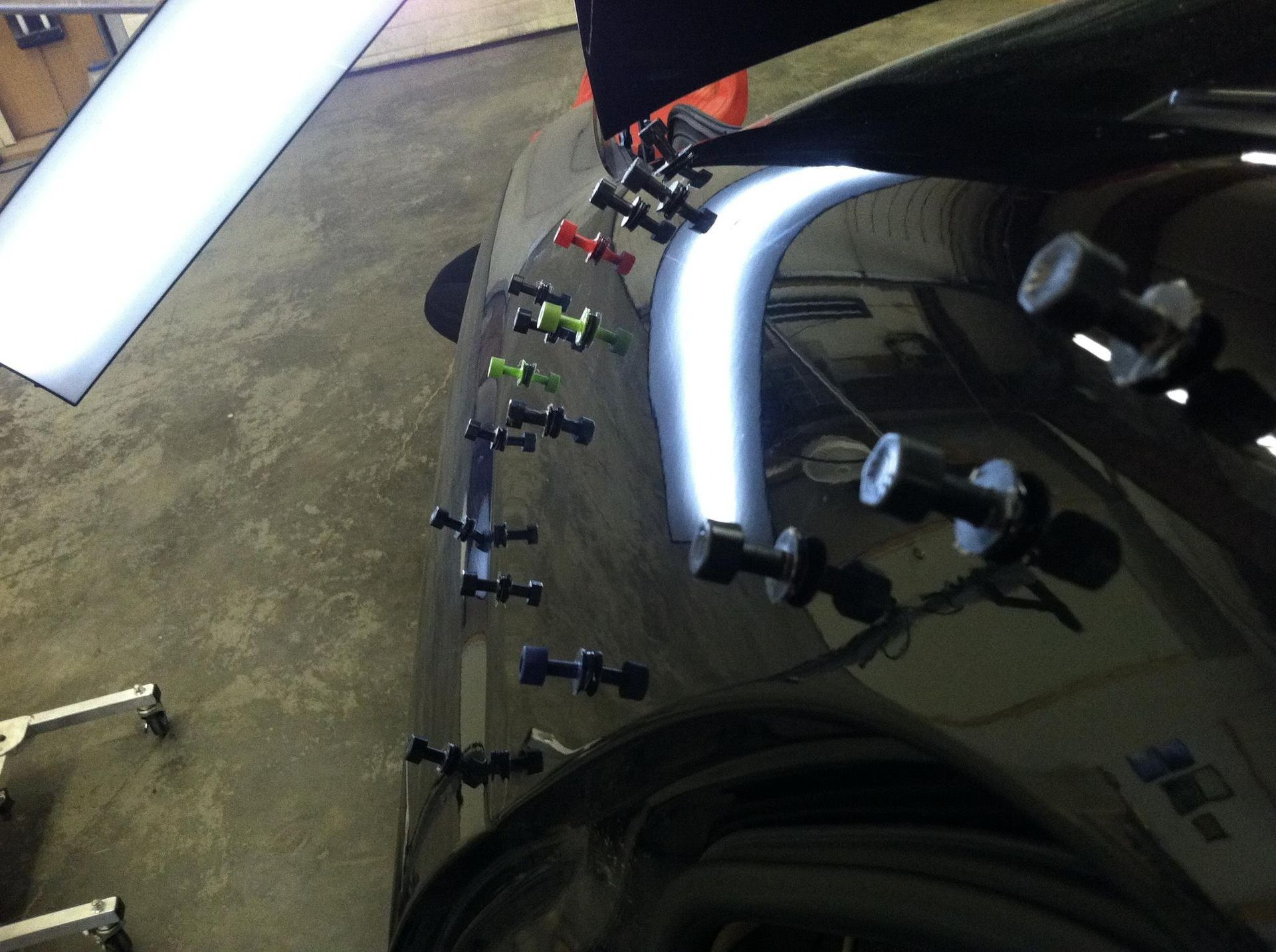 Car wrap being clamped in a workshop, with bright light reflecting on the car body.