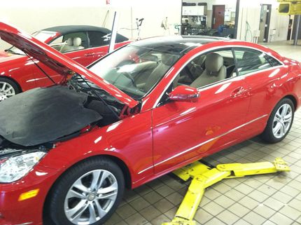 Red car with hood open in a garage, with a yellow jack under the front side.
