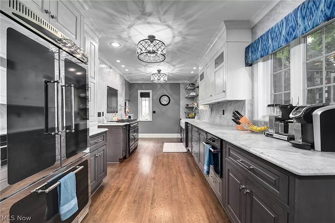 A kitchen with gray cabinets , white cabinets , stainless steel appliances and hardwood floors.