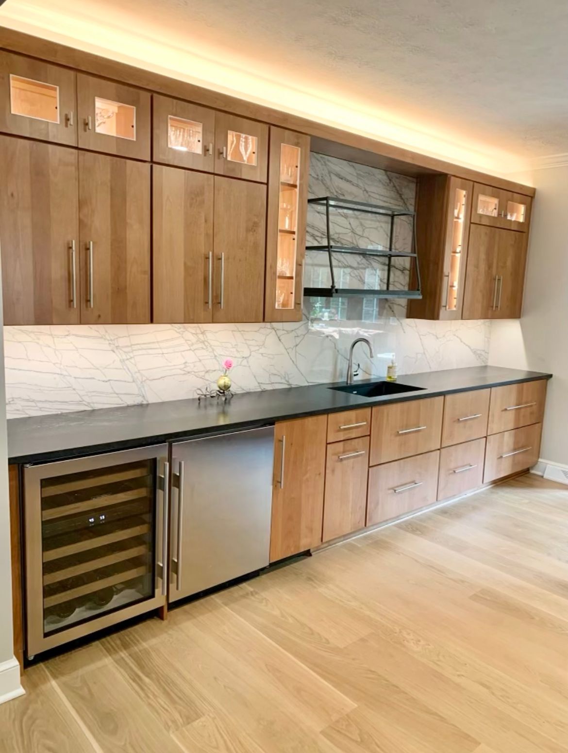 A kitchen with wooden cabinets , stainless steel appliances , a sink , and a wine cooler.
