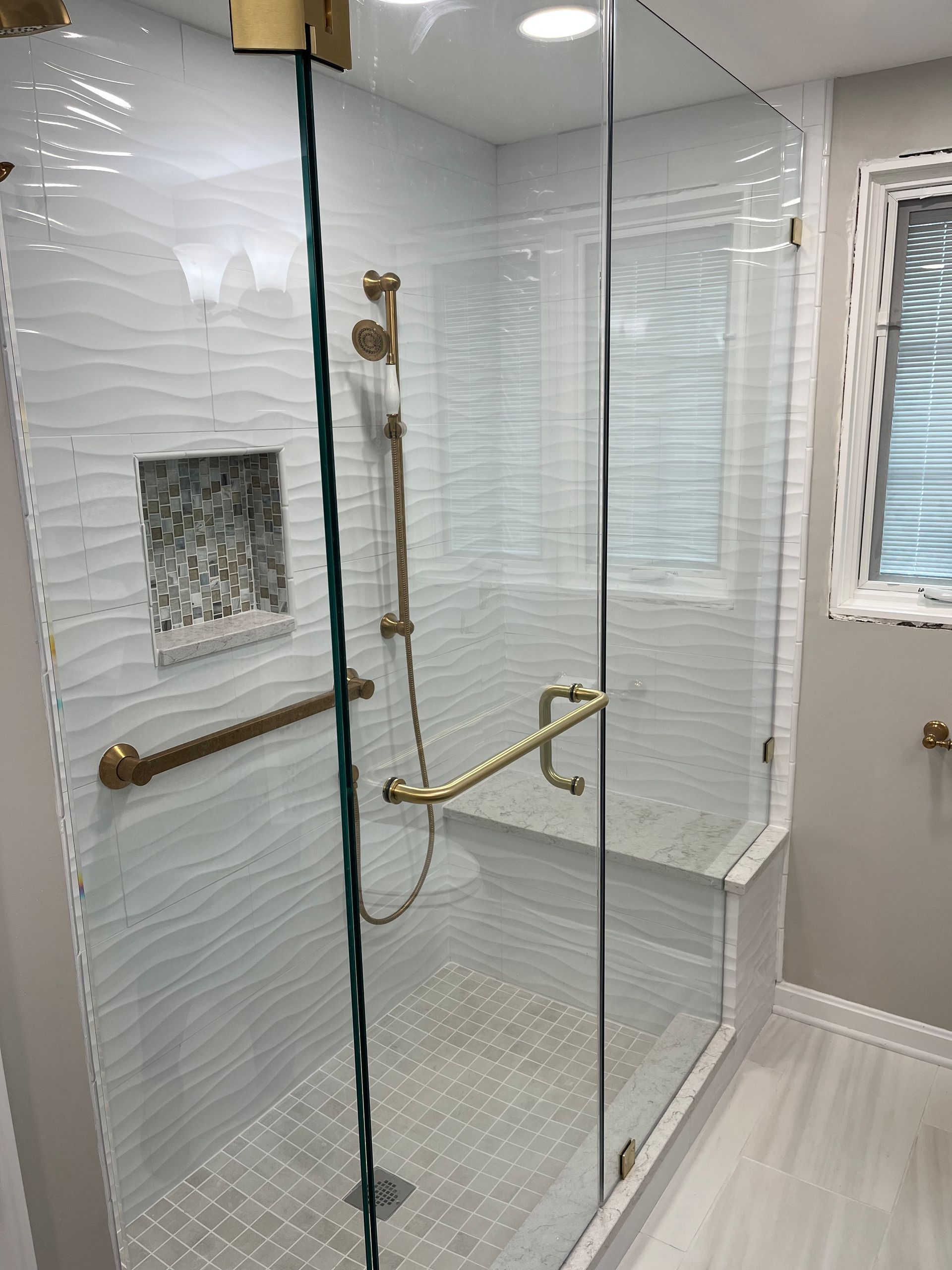 A bathroom with a walk in shower with a glass door and a window.