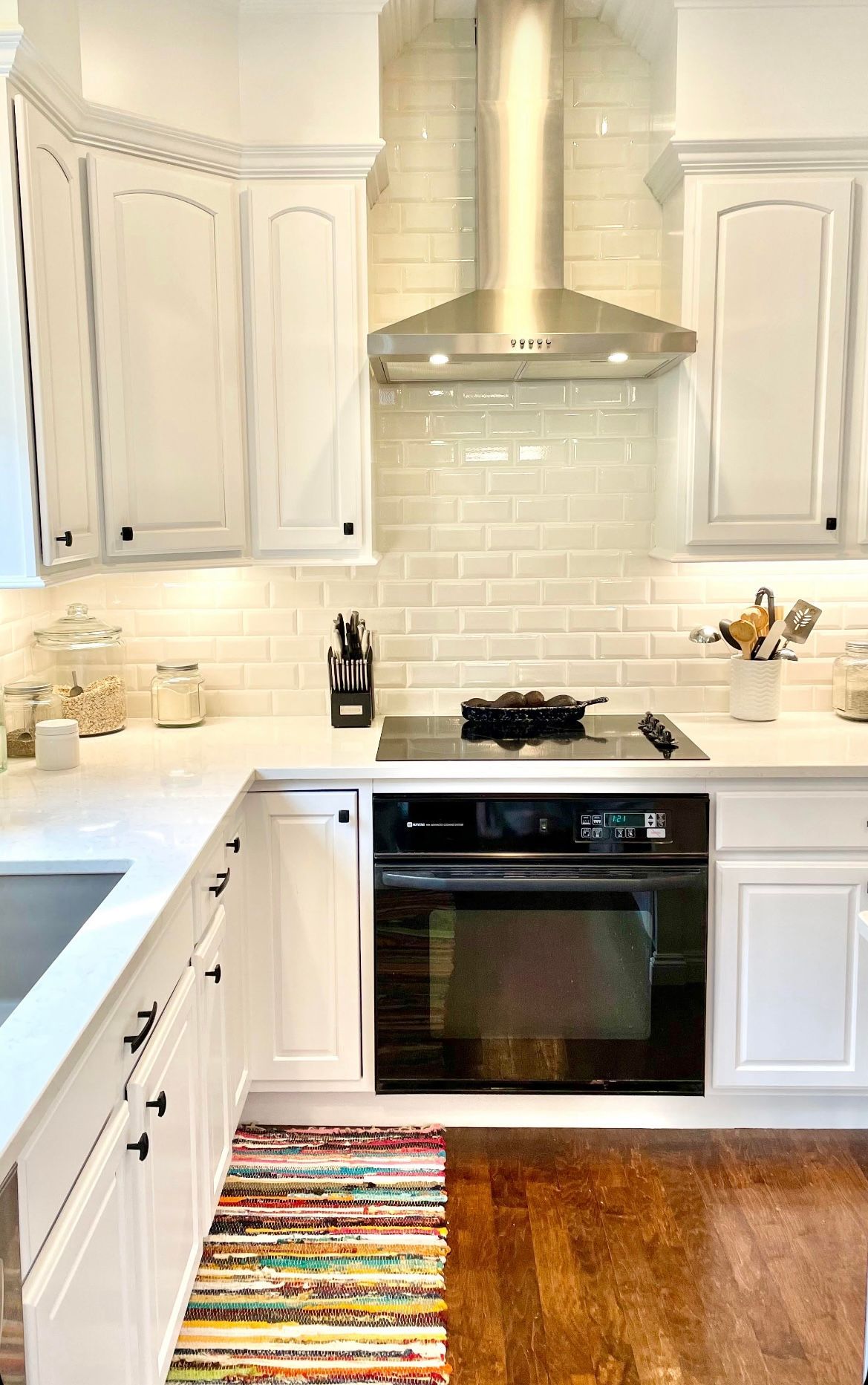 A kitchen with white cabinets , a stove , a sink , and a rug.