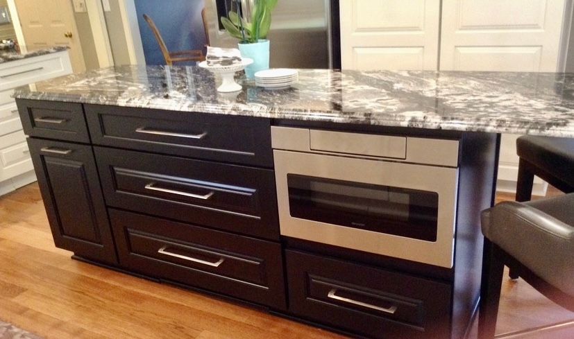 A kitchen island with black cabinets and a stainless steel microwave oven.