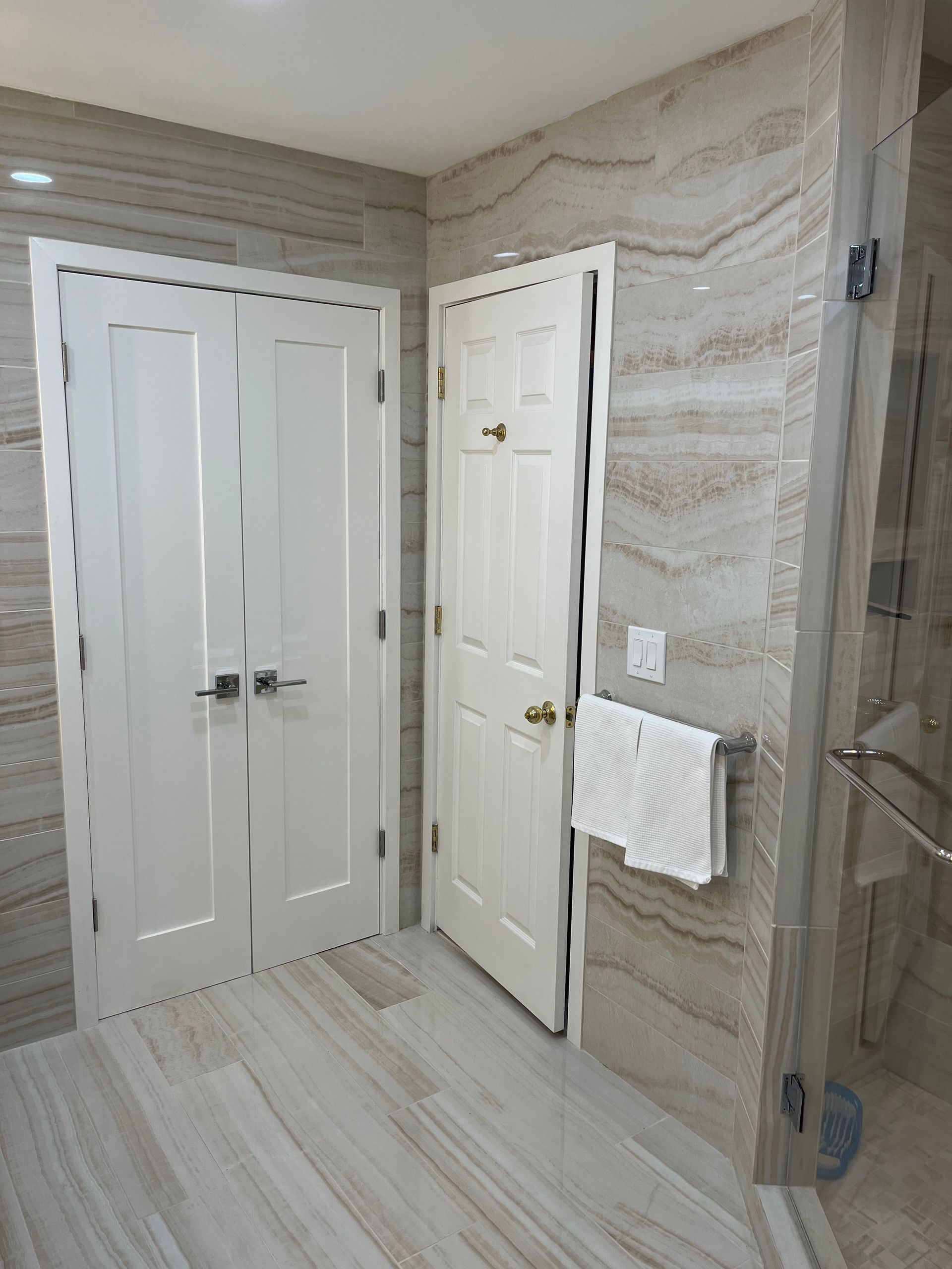 A bathroom with two doors , a shower and a towel rack.