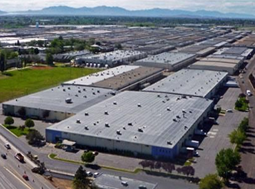 Aerial view of a large industrial warehouse complex with parking lots and distant mountains.