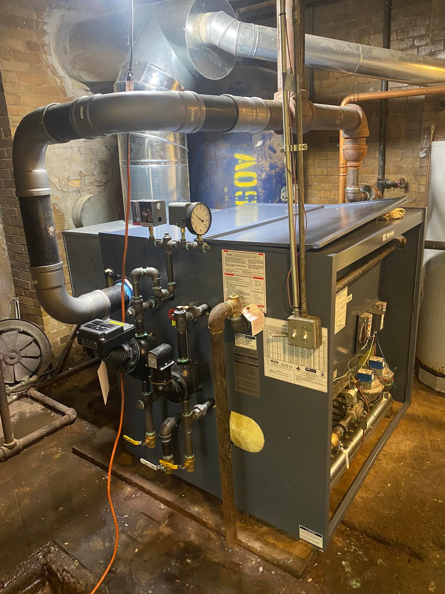 A large boiler is sitting in a basement next to a brick wall.