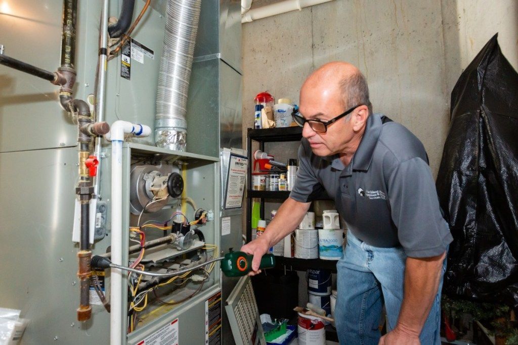 Technician inspects HVAC equipment in a utility room, using a green power drill.