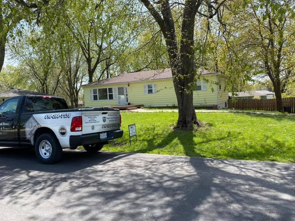 White work truck parked by a yellow house with a large tree and green lawn on a sunny day
