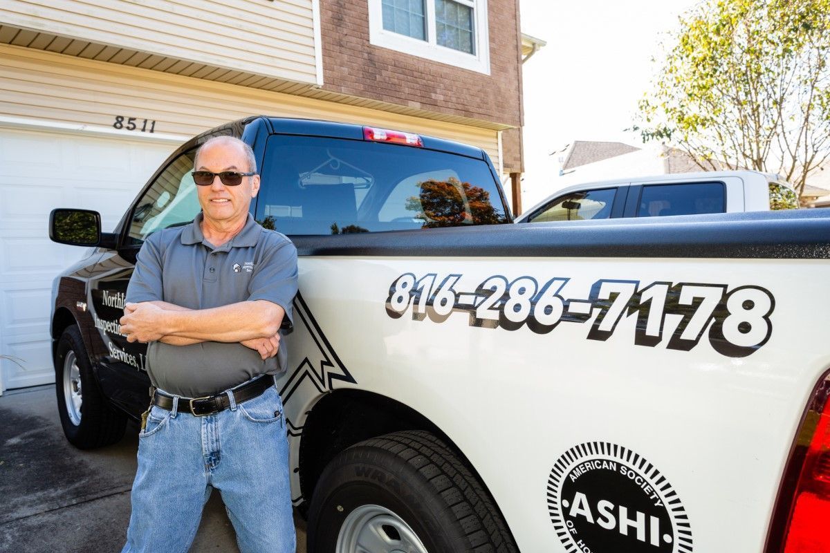 Man standing with arms crossed beside a black-and-white service truck displaying phone number 816-286-7178.