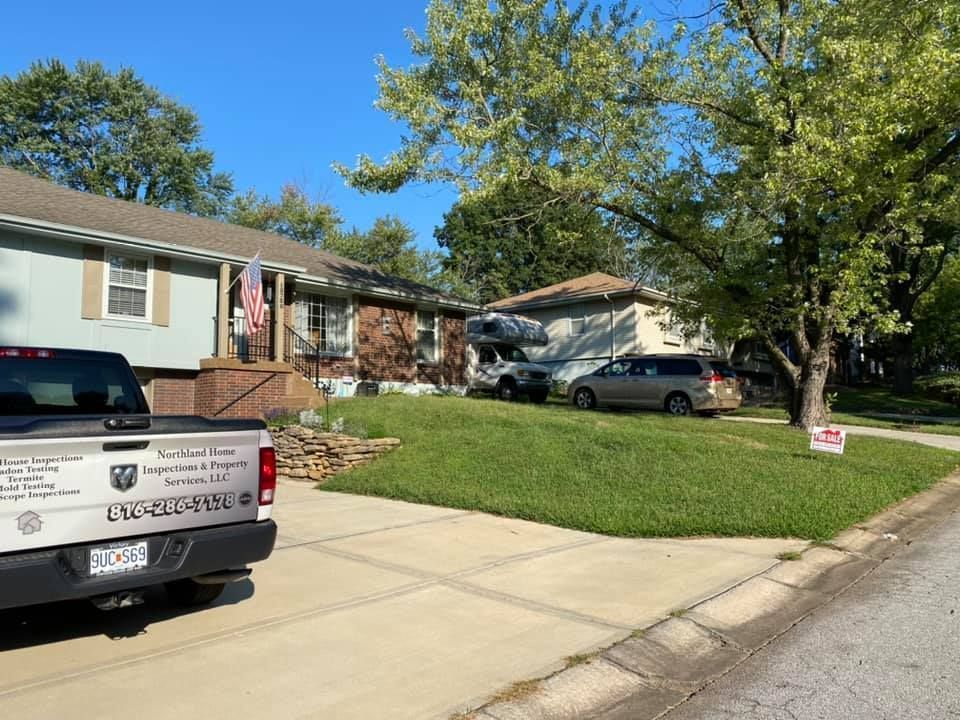 Suburban house with parked vehicles, green lawn, and a white pickup truck in the driveway under a clear blue sky