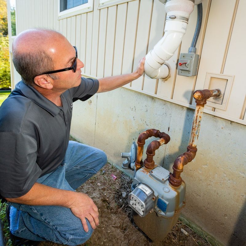 Man inspecting gas meter and white vent pipe beside a house exterior
